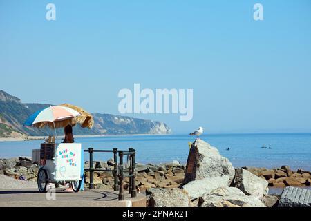 Eisverkäufer auf der Promenade am Ende des Strandes mit Blick auf die Küste, Sidmouth, Devon, Großbritannien, Europa. Stockfoto