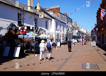 Touristen laufen entlang der Einkaufsstraßen in der Altstadt mit dem Anchor Inn Pub auf der linken Seite, Sidmouth, Devon. Stockfoto