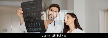 Zwei Ärzte sehen und diskutieren in Uniform eine Röntgen- oder MRT-Untersuchung der Wirbelsäule des Patienten Stockfoto