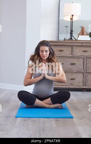 Ich bin ruhig, mein Baby ist ruhig. Eine schwangere junge Frau, die zu Hause meditiert. Stockfoto