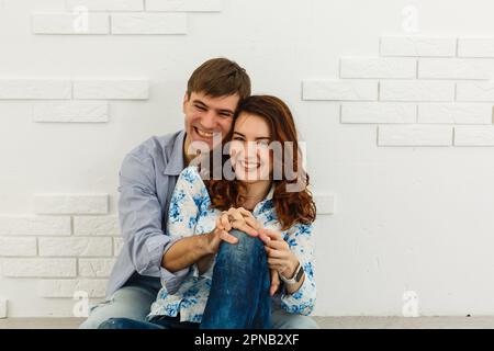 Ein traumhaftes Paar, das auf dem Boden liegt, in einem leeren Raum liegt und aufblickt. Stellen Sie sich ein zukünftiges Innenraumprojekt vor, weißer Hintergrund. Stockfoto