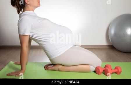 Das Mädchen ist während der Schwangerschaft in Pilates und Sport verwickelt. Übungen mit Sportball und Kurzhanteln. Frauengesundheit, Mutterschaft Stockfoto