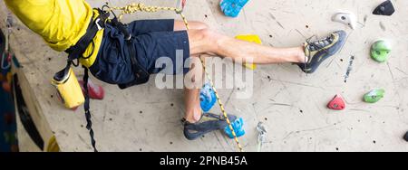 Nahaufnahme eines jungen Mannes oder Kletterfußes in Kletterschuhen an künstlicher Innenwand im Kletterzentrum, Sportkonzept Stockfoto