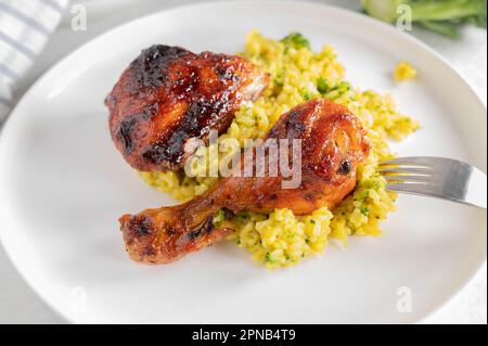 Gegrillte Hähnchenschenkel mit braunem Curryreis und Brokkoli auf einem Teller Stockfoto