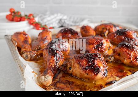 Im Ofen gebackene und glasierte Hähnchenschenkel und Hähnchenschenkel mit Honig-Barbecue-Sauce auf einem Backblech auf dem Küchentisch Stockfoto