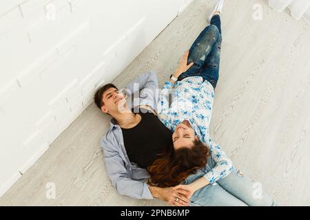 Ein traumhaftes Paar, das auf dem Boden liegt, in einem leeren Raum liegt und aufblickt. Stellen Sie sich ein zukünftiges Innenraumprojekt vor, weißer Hintergrund. Stockfoto