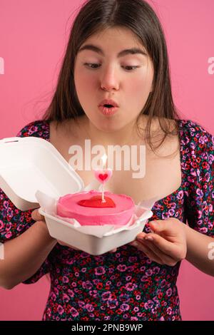 Ein Mädchen bläst die Kerze auf einem pinken Bento-Kuchen aus Stockfoto
