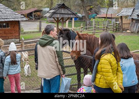 Lemberg, Ukraine. 17. April 2023. Erwachsene und Kinder stehen in der Nähe eines Gehäuses mit Pferden Trotz des Krieges feiern die Menschen den zweiten Ostertag und besuchen den Park mit Vieh, um sie zu füttern, Spaß zu haben und Zeit mit Familienkredit zu verbringen: SOPA Images Limited/Alamy Live News Stockfoto