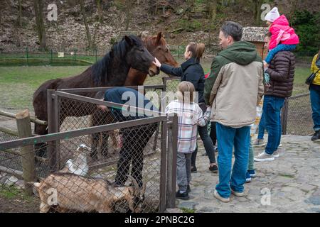 Lemberg, Ukraine. 17. April 2023. Erwachsene und Kinder stehen in der Nähe eines Gehäuses mit Pferden Trotz des Krieges feiern die Menschen den zweiten Ostertag und besuchen den Park mit Vieh, um sie zu füttern, Spaß zu haben und Zeit mit Familienkredit zu verbringen: SOPA Images Limited/Alamy Live News Stockfoto