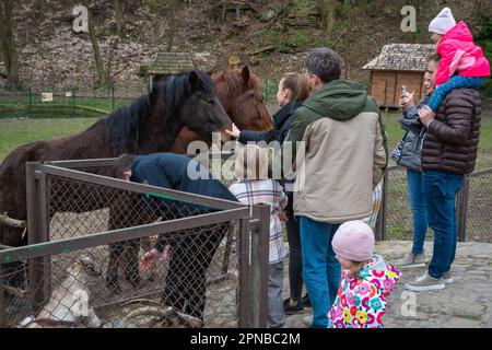 Lemberg, Ukraine. 17. April 2023. Erwachsene und Kinder stehen in der Nähe eines Gehege mit Pferden Trotz des Krieges feiern die Menschen den zweiten Ostertag und besuchen den Park mit Vieh, um sie zu füttern, Spaß zu haben und Zeit mit der Familie zu verbringen. Kredit: SOPA Images Limited/Alamy Live News Stockfoto