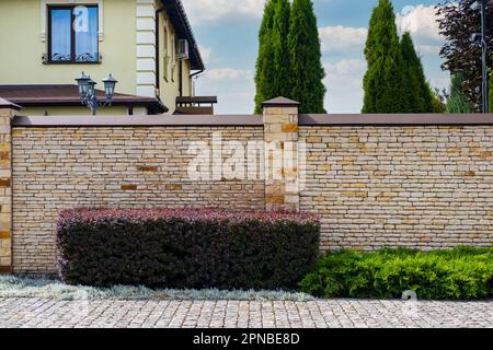 Modernes Backsteinmuster aus heller Steinzaunwand mit Pfosten vor einem Wohngebäude. Stockfoto