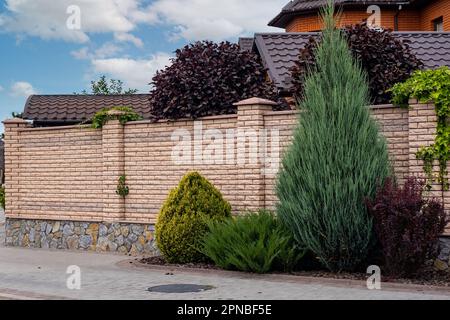 Modernes Backsteinmuster aus heller Steinzaunwand mit Pfosten vor einem Wohngebäude. Stockfoto