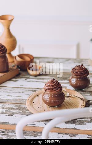 Köstliche süße Schokoladenmousse-Desserts in Glasgläsern mit Besteck auf Holztisch vor weißem Hintergrund Stockfoto