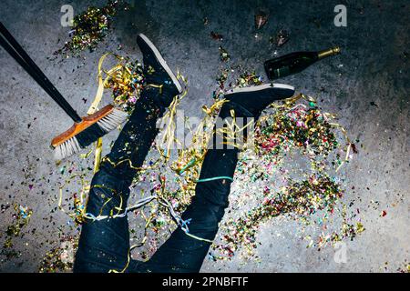 Draufsicht auf den anonymen Mann, der während der Festtage mit farbigen Papierstreamern und einer Flasche Champagner auf dem Boden liegt Stockfoto