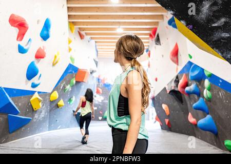 Seitenansicht junger anonymer Freundinnen, die auf die Kletterwände mit farbcodierten Griffen im Fitnessstudio blicken Stockfoto