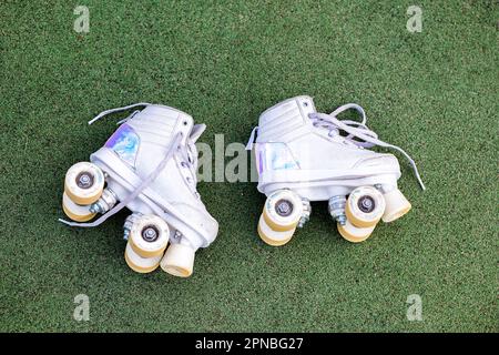 Draufsicht auf glänzende Sneaker in weiß-blau-rosa Farben und mit Schnürsenkeln auf grünem Gras bei Tageslicht mit Rollschuhen Stockfoto