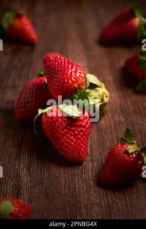 Zusammensetzung frischer, appetitlicher Erdbeeren mit grünen Blättern, die im Haufen auf Holzfläche angeordnet sind Stockfoto