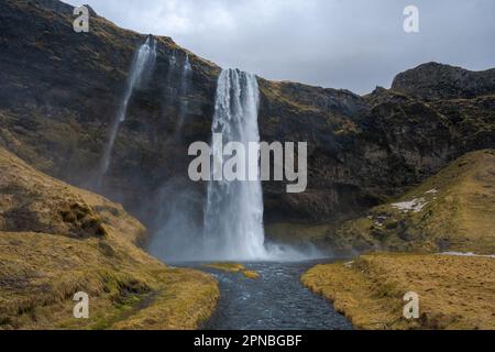 Malerischer Blick auf den Wasserfall Seljalandsfoss, der von rauen Felsen in den Fluss stürzt und Felsen in bergigen Wäldern in Island hinunterfließt Stockfoto