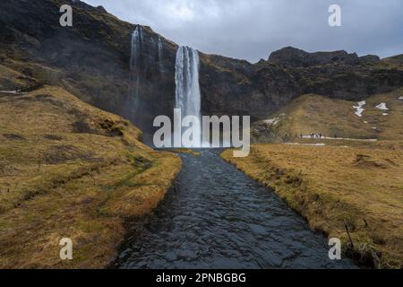 Malerischer Blick auf den Wasserfall Seljalandsfoss, der von rauen Felsen in den Fluss stürzt und Felsen in bergigen Wäldern in Island hinunterfließt Stockfoto