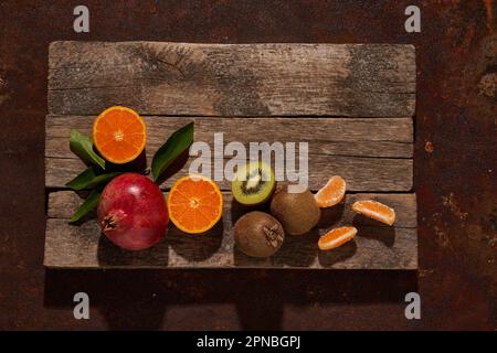 Blick von oben auf frische, reife Kiwi- und Orangenscheiben in der Nähe von Granatäpfeln, die auf Holzbrettern angeordnet sind Stockfoto