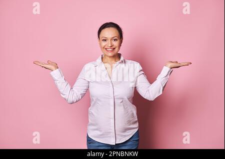 Glückliche lächelnde schwangere Frau, die in die Kamera schaut und imaginären Kopierraum auf ihren Händen hält Stockfoto