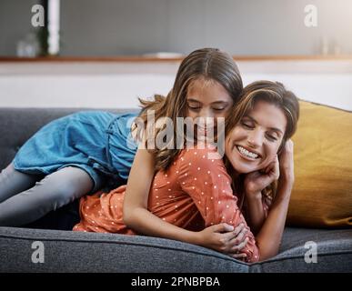 Es gibt nichts Schöneres als eine Mütterliebe. Eine attraktive junge Frau und ihre Tochter, die sich umarmen, während sie zu Hause Zeit miteinander verbringen. Stockfoto