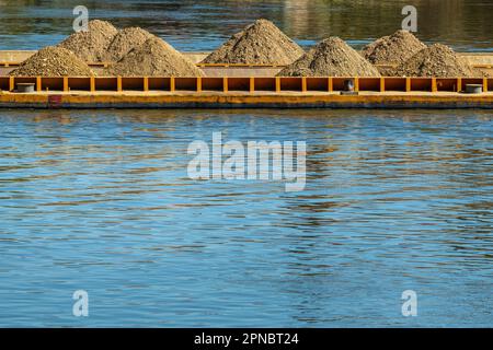 Ein Boot mit flachem Boden, das von einem Schlepper entlang des Flusses geschoben wird, um Kies und Sand zu transportieren. Selektiver Fokus. Stockfoto