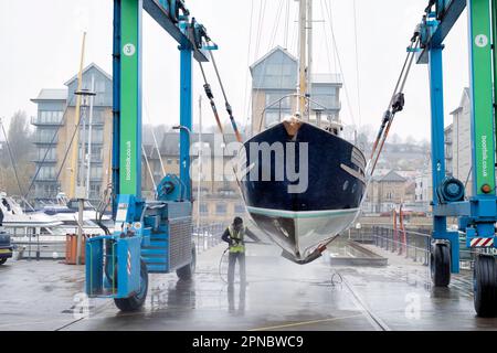 Eine weibliche Wartungsfirma reinigt den Rumpf eines Boots, das in Portishead Marina UK aus dem Wasser gehoben wurde. Das Boot wird in einem „Wise Boat Hoist“ gehalten Stockfoto