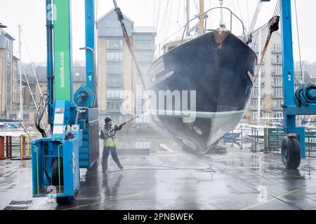 Eine weibliche Wartungsfirma reinigt den Rumpf eines Boots, das in Portishead Marina UK aus dem Wasser gehoben wurde. Das Boot wird in einem „Wise Boat Hoist“ gehalten Stockfoto