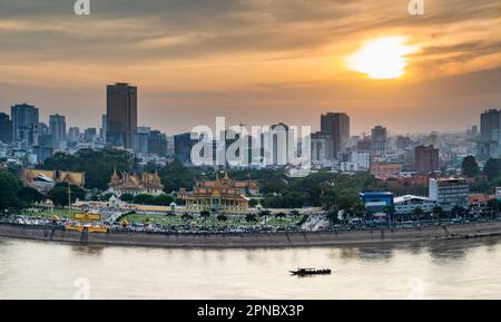 Blick auf das Dach, Blick auf die Flussgegend von Kambodschas Hauptstadt. Sonnenuntergang über dem Königspalast und den Hochhäusern dahinter, als kleines Boot Stockfoto