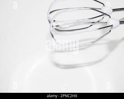 Weißer Schaum aus Konditorcreme aus Eiern und Zucker auf den Quirlen eines Mischers. Selektiver Fokus. Nahaufnahme. Stockfoto