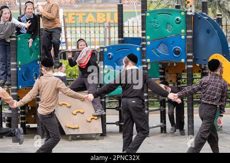 Eine Gruppe von Schülerinnen und Schülern, die ihre Pause in einem kleinen Park auf der anderen Straßenseite von ihrer Jeschiwa genießen. In Brooklyn, New York. Stockfoto