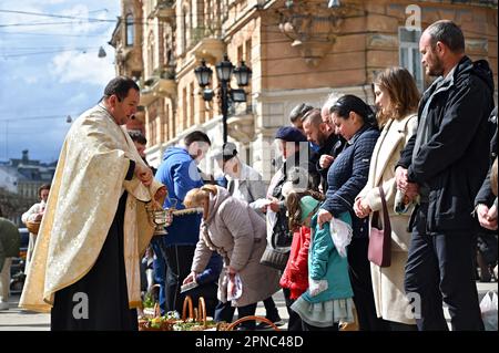 LEMBERG, UKRAINE - 15. APRIL 2023 - Ein Priester segnet Gläubige und ihre Osterkörbe mit Weihwasser vor dem Bernardinenkloster am Heiligen Samstag, Stockfoto