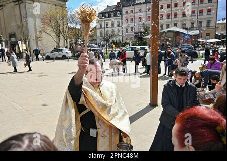 LEMBERG, UKRAINE - 15. APRIL 2023 - Ein Priester segnet Gläubige und ihre Osterkörbe mit Weihwasser vor dem Bernardinenkloster am Heiligen Samstag, Stockfoto