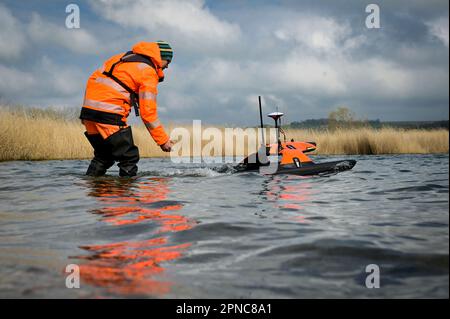 Aseleben, Deutschland. 18. April 2023. Stephan Packebusch stellt die schwimmende Drohne Sonobot ins Wasser. Das Gerät kann dann den Seegrund mit Sonar unabhängig voneinander scannen und anzeigen. Diese moderne Technologie wird zum ersten Mal bei der Suche nach archäologischen Schätzen unter Wasser auf dem Grund des Lake Suess eingesetzt. Kredit: Heiko Rebsch/dpa/Alamy Live News Stockfoto