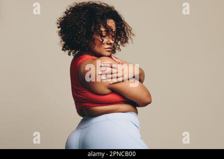 Fit junge Frau umarmt ihren Körper in einem Sportswear-Outfit und strahlt körperliche Positivität und Selbstliebe aus. Große Frau mit sportlicher Note Stockfoto