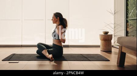 Glückliche Seniorin, die während einer Hatha-Yoga-Sitzung die Kuhgesicht-Pose macht. Reife Frau, die eine Dehnübungen auf einer Yogamatte macht. Senior-Frauen-Praktikum Stockfoto