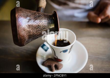 Die Person schüttet während einer östlichen traditionellen Trinkzeremonie traditionellen türkischen Kaffee in eine Tasse Stockfoto