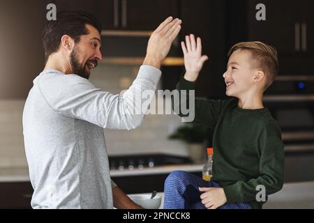 Er wollte immer Vater werden. Ein gutaussehender junger Mann und sein Sohn High Five in der Küche. Stockfoto