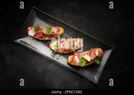 Köstliches Bruschetta garniert mit geräuchertem Lachs, Schinken und Parmesan Stockfoto