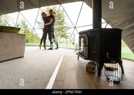 Ein Paar, das die Natur aus Geo-Dome-Zelten betrachtet. Grün, blau, orangefarbener Hintergrund. Gemütlich, Camping, Glamping, Urlaub, Urlaub Lifestyle Konzept. Malerisch Stockfoto