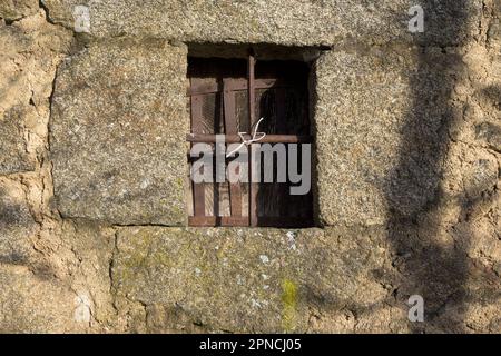 Kleines Holzfenster mit rostigem schmiedeeisernen Zaun in einer Steinwand Stockfoto