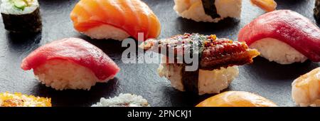 Sushi-Panorama. Nigiri mit Aal, Thunfisch, Lachs auf schwarzem Hintergrund, japanisches Essen auf einem Teller in einem asiatischen Restaurant Stockfoto