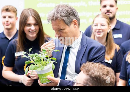 Hannover, Deutschland. 18. April 2023. Robert Habeck (Bündnis 90/die Grünen, 3. von links), Bundesminister für Wirtschaft und Klimaschutz, steht am ebm-Papst-Stand während einer Führung durch die Hannover Messe und hält einen Blumentopf mit einem grünen Kräuter in den Händen. Daneben sind ebm-päpstliche Auszubildende. Vom 17. Bis 21. April 2023 findet die weltweit größte Industriemesse statt. Kredit: Michael Matthey/dpa/Alamy Live News Stockfoto