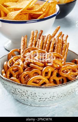 Eine Schüssel mit salzigen Snacks aus nächster Nähe. Partymischung mit Brezeln und Stäbchen, mit Kartoffelchips im Hintergrund Stockfoto