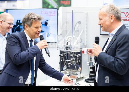 Hannover, Deutschland. 18. April 2023. Robert Habeck (Bündnis 90/die Grünen, 2. von links), Bundesminister für Wirtschaft und Klimaschutz, steht vor einer hydraulischen Kaffeemaschine während einer Führung durch den HAWE Hydraulik-Stand auf der Hannover Messe. Neben ihm steht Karl Haeusgen (r), Präsident des Deutschen Ingenieurverbands. Vom 17. Bis 21. April 2023 findet die weltweit größte Industriemesse statt. Kredit: Michael Matthey/dpa/Alamy Live News Stockfoto