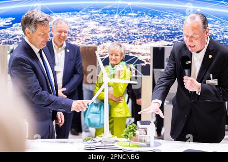 Hannover, Deutschland. 18. April 2023. Robert Habeck (Bündnis 90/die Grünen, l), Bundesminister für Wirtschaft und Klimaschutz, steht vor einem Modell einer Windturbine während einer Führung durch den Stand von Phoenix Contact auf der Hannover Messe. Daneben stehen die Mitarbeiter Klaus Hengsbach (2. von links), Angela Josephs (M) und Frank Stührenberg (r), CEO Phoenix Contact. Vom 17. Bis 21. April 2023 findet die weltweit größte Industriemesse statt. Kredit: Michael Matthey/dpa/Alamy Live News Stockfoto