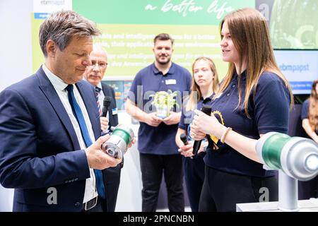 Hannover, Deutschland. 18. April 2023. Robert Habeck (Bündnis 90/die Grünen, l), Bundesminister für Wirtschaft und Klimaschutz, steht am Stand von ebm-Papst auf einer Führung durch die Hannover Messe und hält einen Turbokompressor in seinen Händen. Dies wird beispielsweise in Brennstoffzellen verwendet. Daneben befinden sich Thomas Wagner (2. von links), COO ebm-Papst und die Praktikanten Melanie Bildhoff (r), Kim Ziegler (2. von rechts) und Maximilian Chrzan (3. von rechts). Vom 17. Bis 21. April 2023 findet die weltweit größte Industriemesse statt. Kredit: Michael Matthey/dpa/Alamy Live News Stockfoto