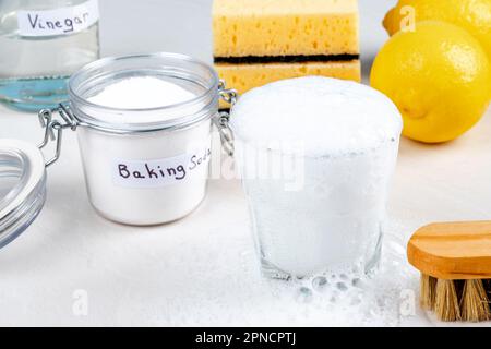 Reaktion zwischen Backnatron aus einem Essiglöffel in einem Glas mit Aktivschaum. Umweltfreundliche Naturreiniger. Isoliert. Stockfoto