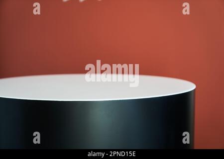 Weiße und schwarze runde Podiumschablone an der roten Wand. Leeres Produktdisplay für Ihre Werbepräsentation. Vorderansicht. Speicherplatz kopieren. Hochwertiges Foto Stockfoto